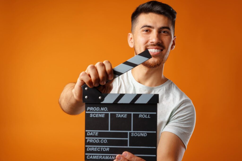 young man holding film clapper board against yellow background